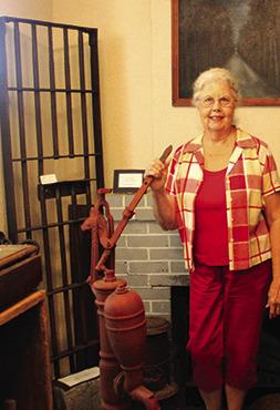 Museum of Hardin County volunteer Susan Cole has her right hand on an old fashioned water pump. To her right are bars from an old jail in Kountze.These are just many of the items from the past which are located in the museum.