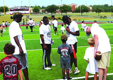 Kalon“Boogie”Barnes,looking down at the boy wearing aT-shirt,was assisted by others in the first annual football camp held last Saturday at Tiger Stadium. Danny Reneau photo