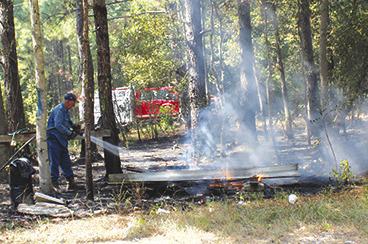 Kountze Firefighter George Stutts extinguishes one of several spot fires created by outdoor burning at 1602 Gandy Road about seven miles northwest of Kountze last Thursday afternoon. Firefighters from Kountze and Silsbee battled the flame with temperatures well above 100 degrees. Two firefighters were treated and one of them was taken to a hospital. Dan Eakin Photo